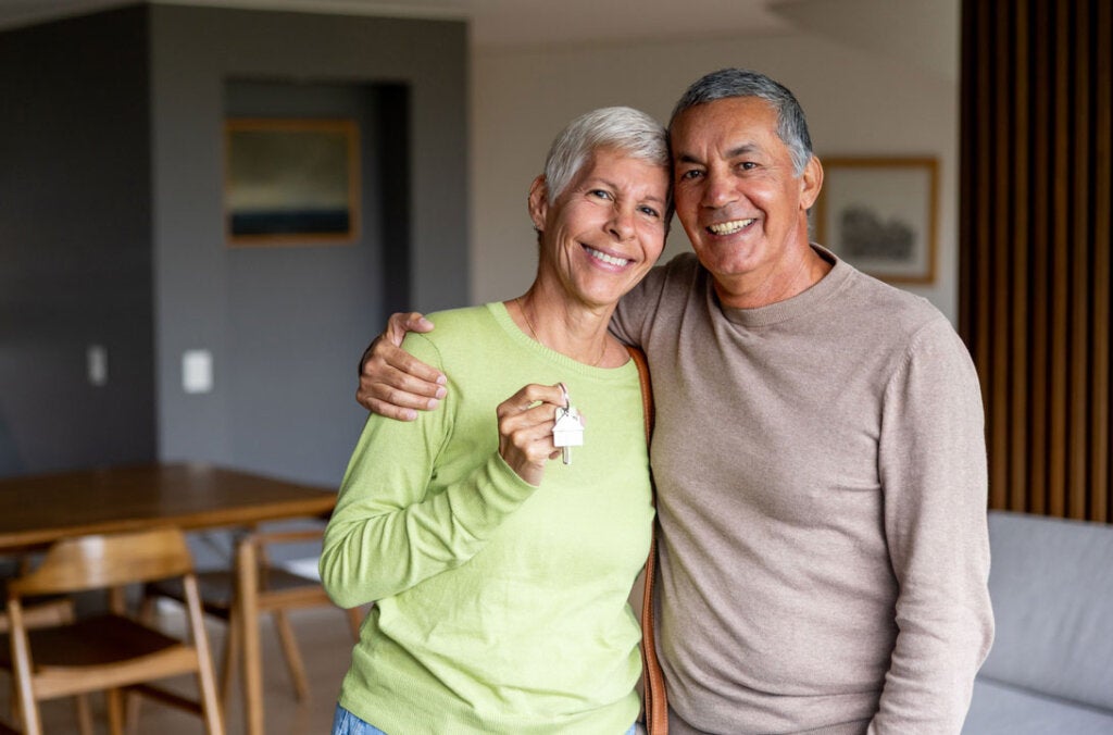 Mature Latin American couple holding the keys of their new house and looking at the camera smiling - home ownership concepts