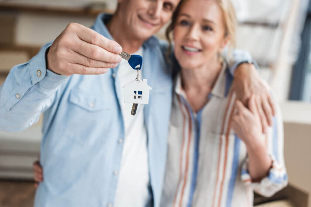 new-house-keys-couple-hugging Close-up view of happy elderly couple holding keys from new nome during relocation
