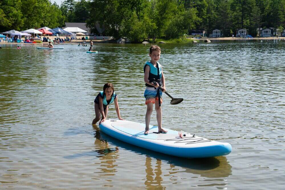 Two kids paddle boarding on Sebago Lake in Maine.