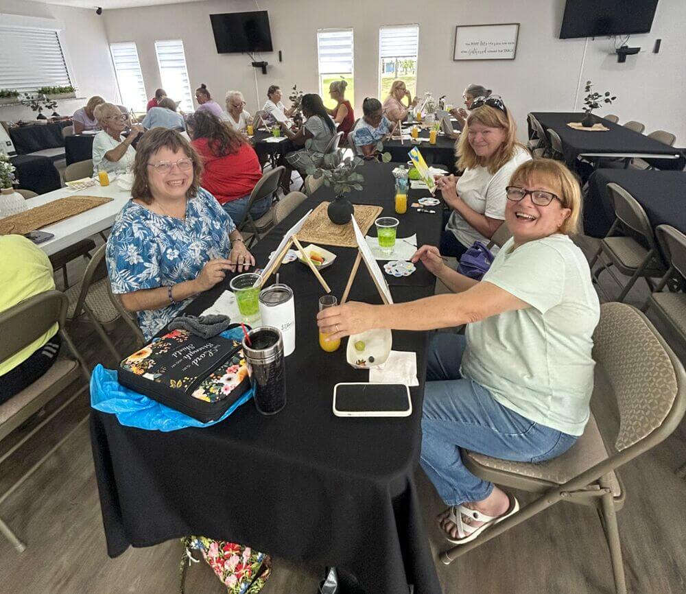 Residents painting canvases and drinking mimosas at a paint and sip event in the West Clubhouse at Rolling Greens Village in Ocala, Florida.