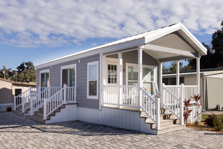 A park model home for sale at Oak Harbor RV Park in Florida. The home is gray and features a front porch.