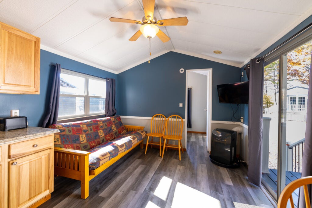 Living space with futon, air conditioner, door to bedroom and sliding glass door to a deck.