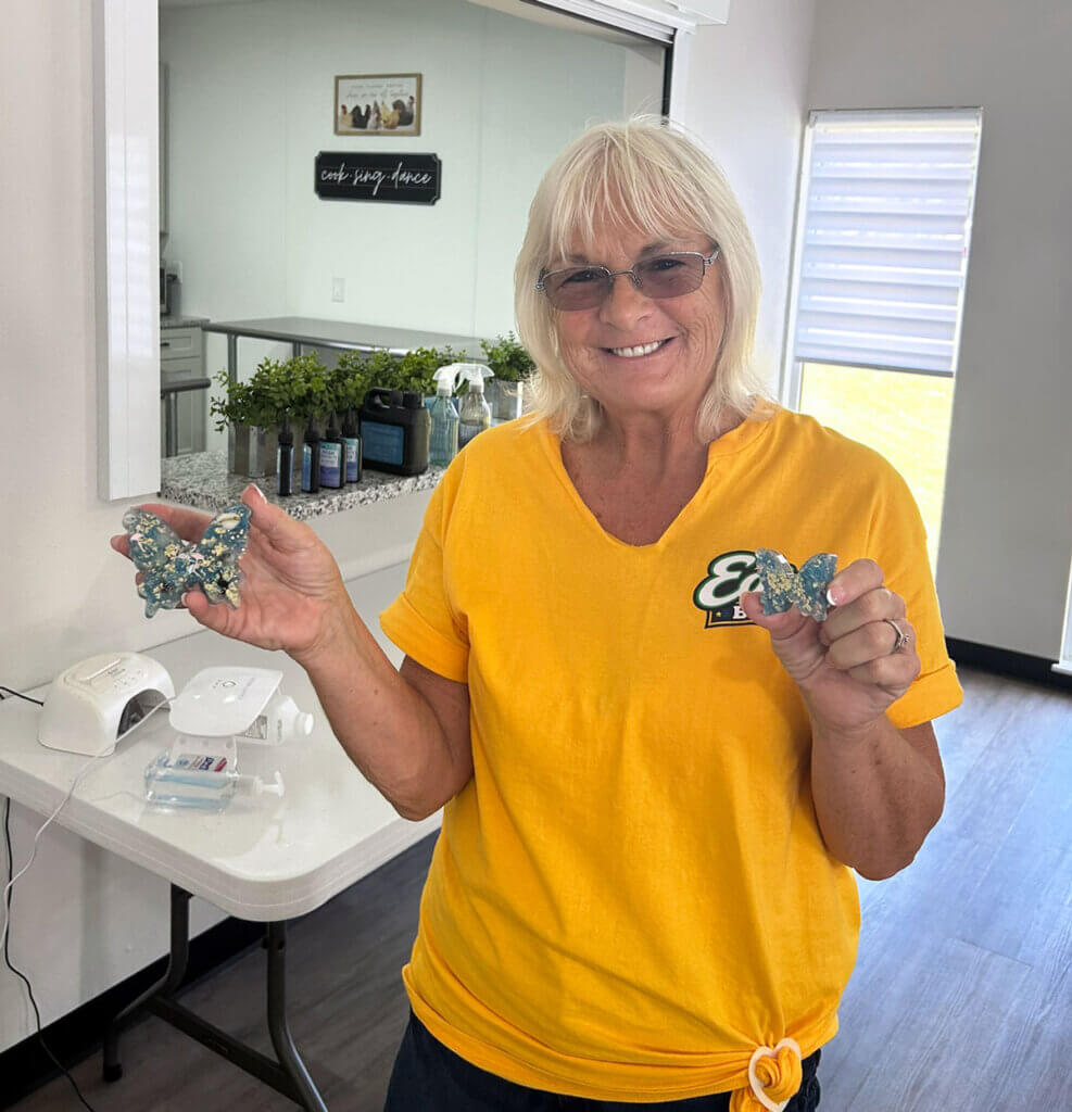 Residents holding two butterfly resin art crafts in the West Clubhouse at Rolling Greens Village in Ocala, Florida.
