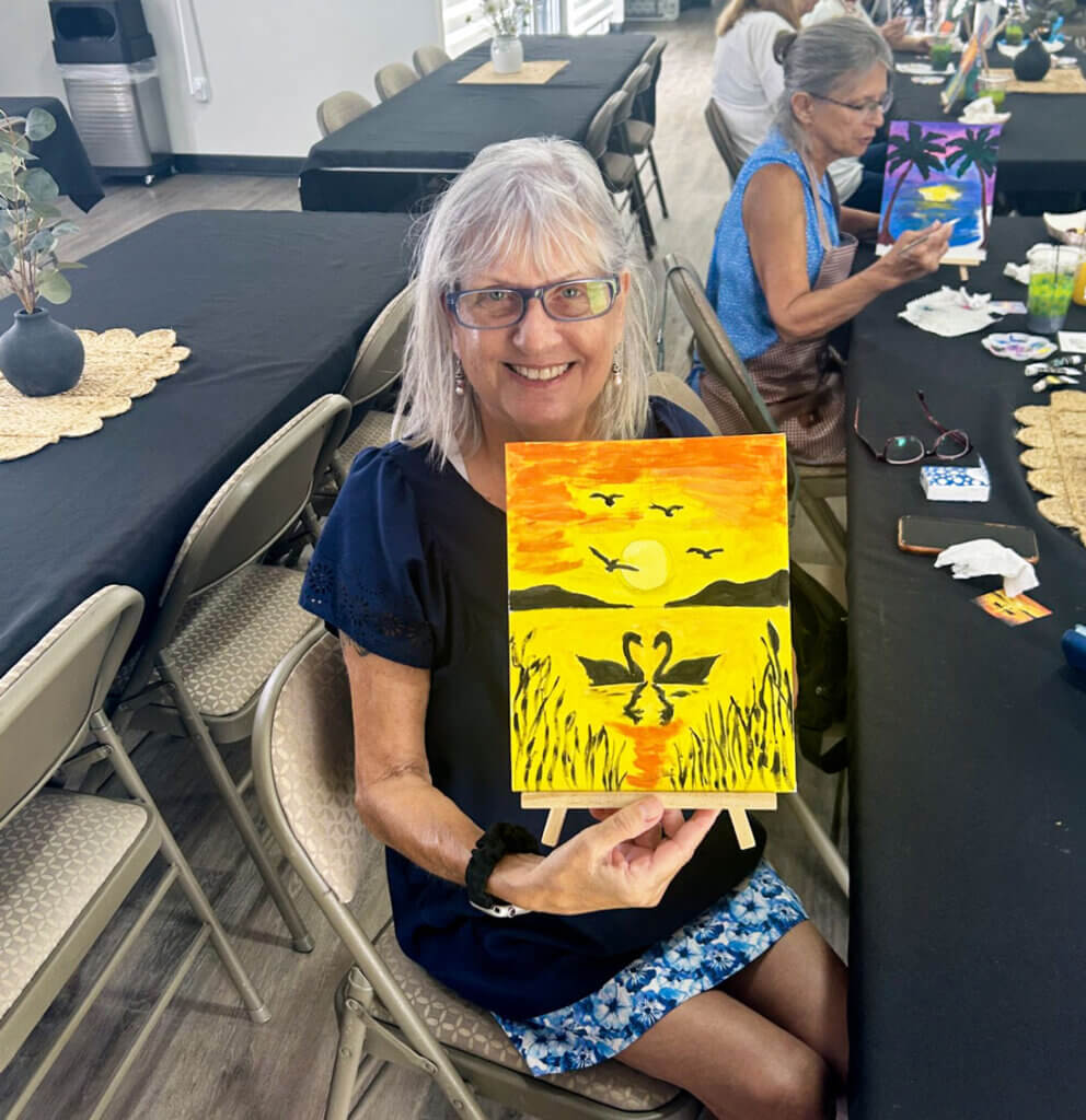 Residents painting canvases and drinking mimosas at a paint and sip event in the West Clubhouse at Rolling Greens Village in Ocala, Florida.