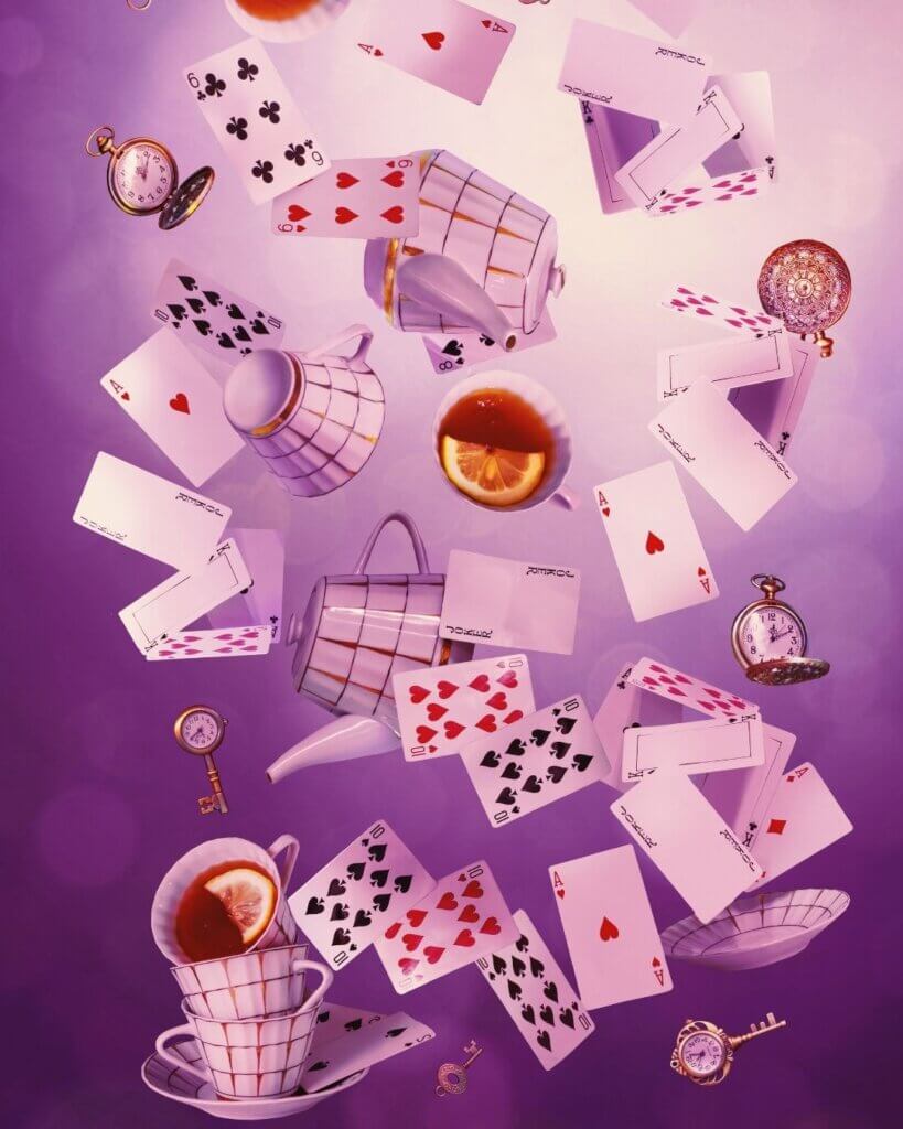 A whimsical scene with playing cards, teacups, teapots, keys, and pocket watches falling against a blurred purple background.