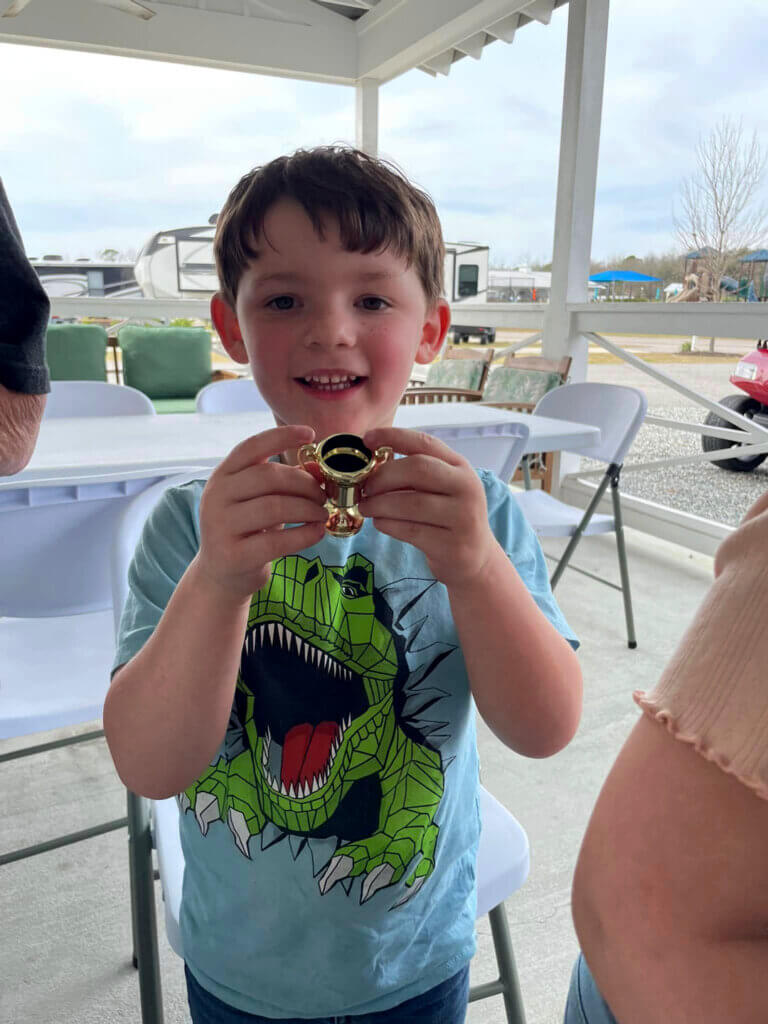 Young boy at CreekFire RV Park wearing a dinosaur shirt holding a mini trophy.