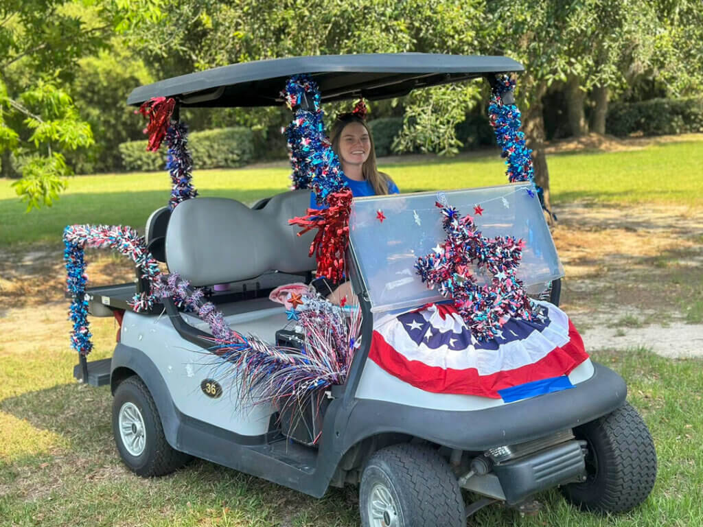 Girl driving golf cart decorated in red white and blue for the memorial day weekend golf cart parade at CreekFire RV Resort.