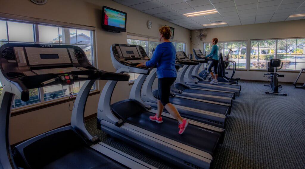 two senior ladies in the fitness center using the elliptical machine and treadmill