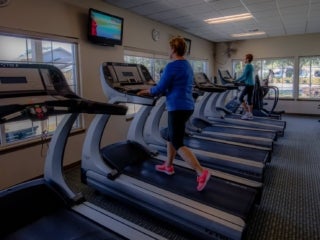 two senior ladies in the fitness center using the elliptical machine and treadmill
