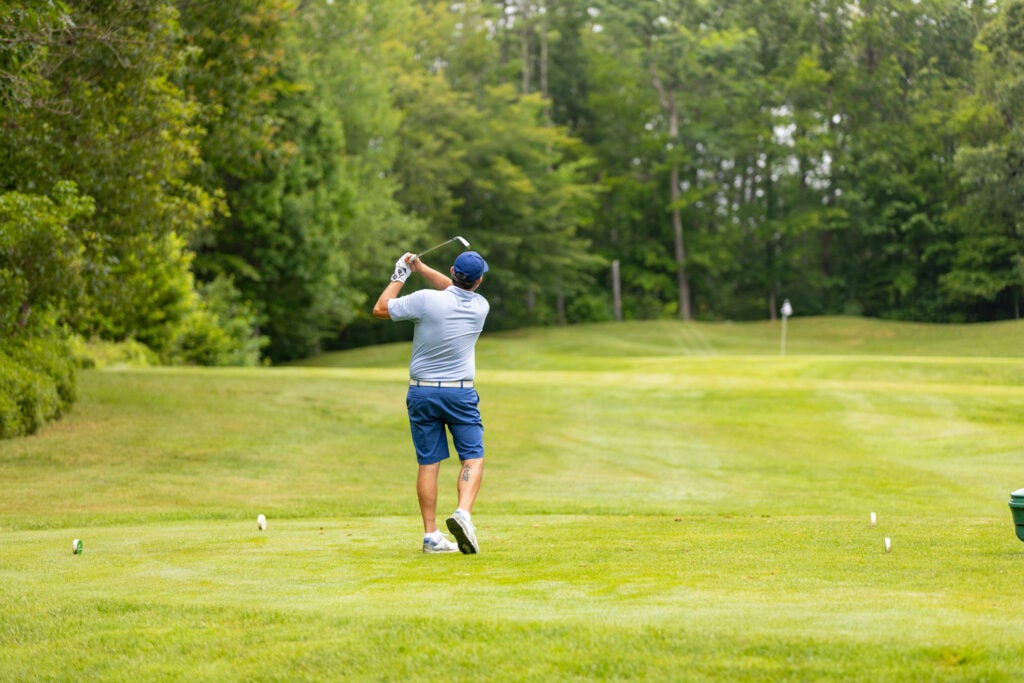 Man hitting golf ball from tee with flag in background