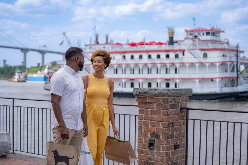 Couple holding shopping bags with the Savannah riverboat in the background in Georgia.