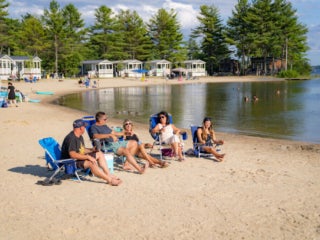 Six friends sitting in beach chairs on the shores of Sebago Lake at Point Sebago Resort in Maine.