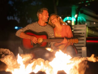 Guitar_Bonfire_Big_Pine_Couple Man playing the guitar with a woman next to him. Both people are next to the bonfire at Big Pine Key RV Park in Florida.