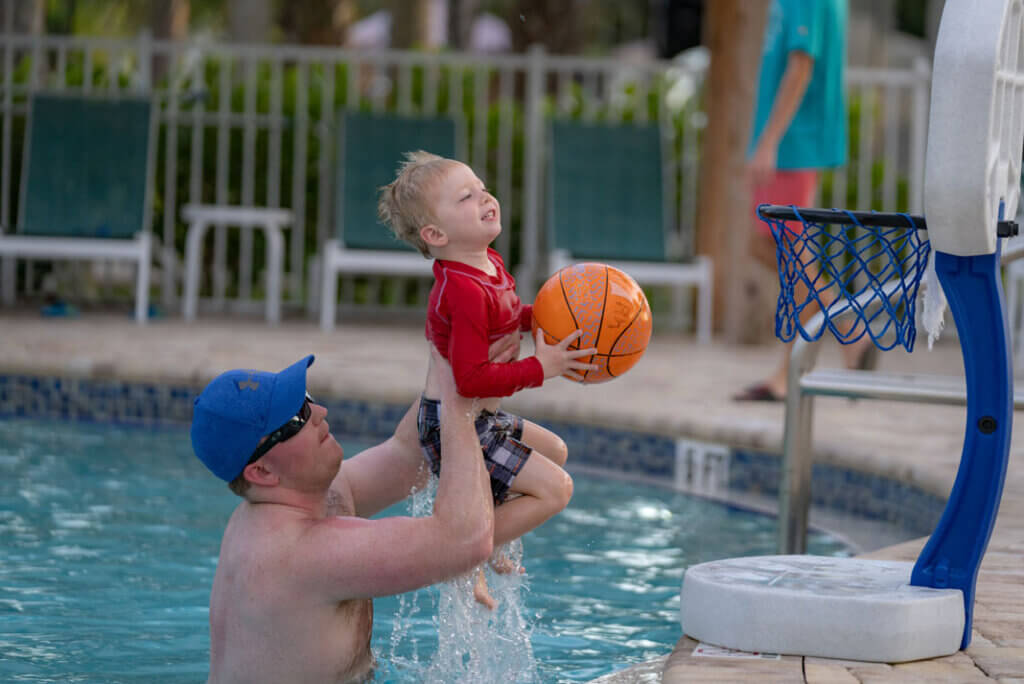 Little boy being lift to the swimming pool basketball court by his dad at Blueway RV Park in Fort Myers, Florida.