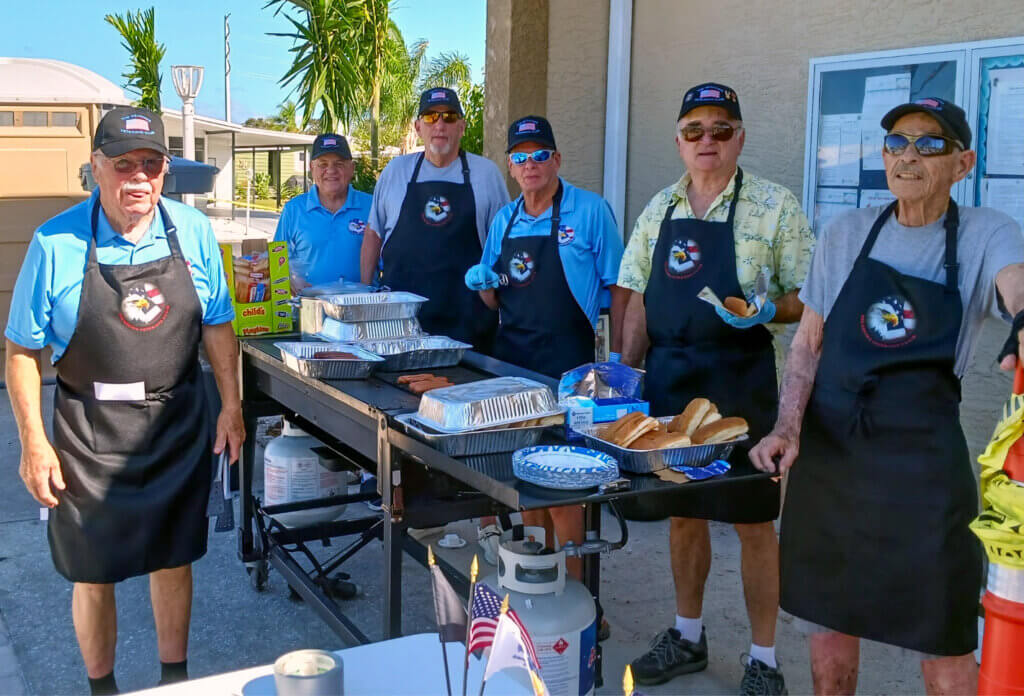 5 members of The Meadows Veteran Club in veterans club aprons grilling hot dogs