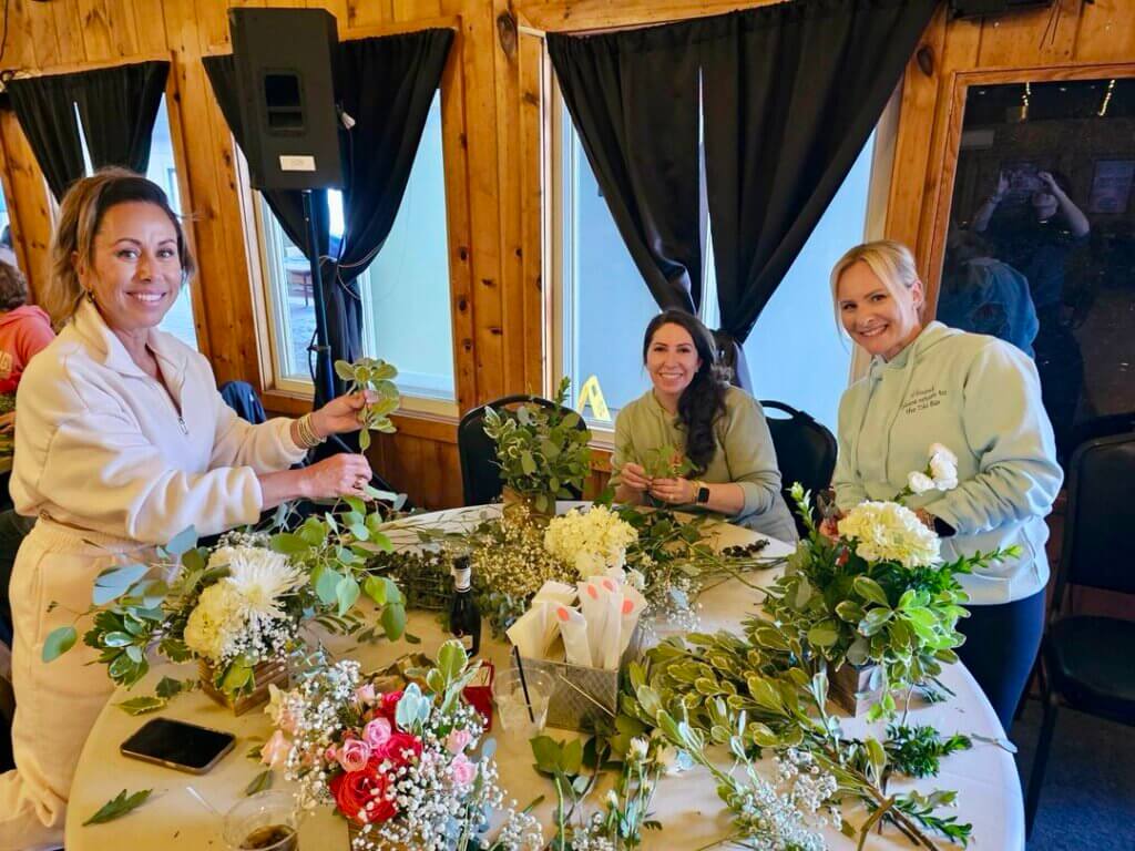 Three women making bouquets in a Point Sebago Resort floral arrangement class in Maine.