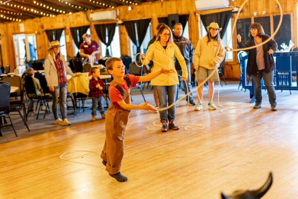 A boy swinging his lasso around at Point Sebago Resort during Country Western Weekend while adults watch.