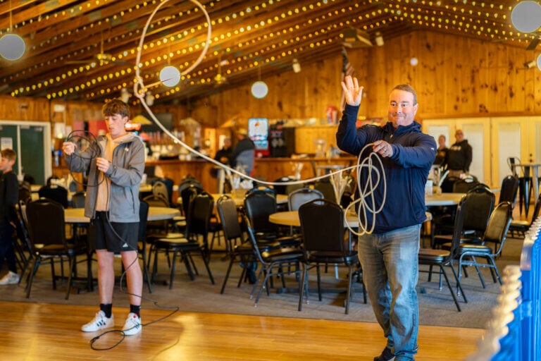 A teenager and a man learning to lasso at Point Sebago Resort during Country Western Weekend.