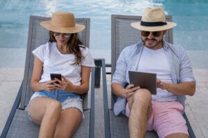 Young millennial couple on their summer holidays relaxing by the pool checking their social media online - lifestyle concepts