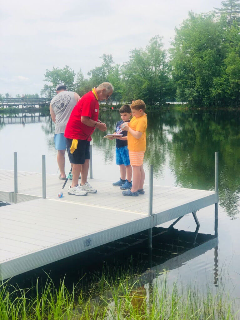 Ranger Rick teachers two boys how to fish on the dock at Point Sebago Resort in Casco, Maine