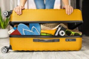 A yellow suitcase with flip flops, a camera, hat, and clothing stuff inside