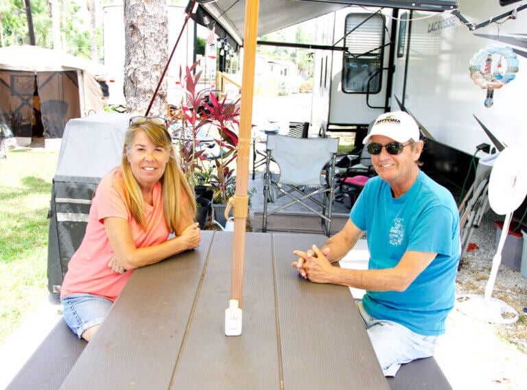 Full Time Blueway Guests Laurie Byrne and Roger Ferreira at a picnic table in front of their RV.