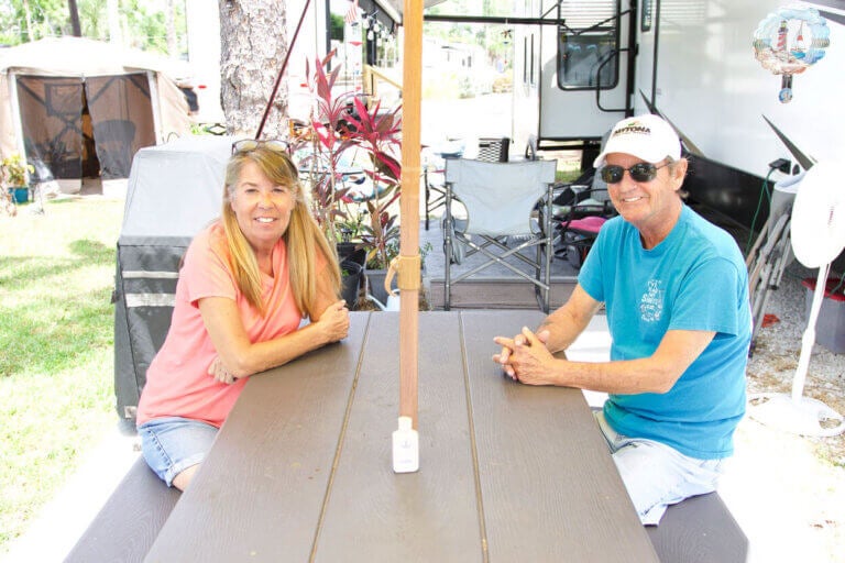 Fulltime Blueway RV Park guests Laurie Byrne and Roger Ferreira at a picnic table in front of their RV.