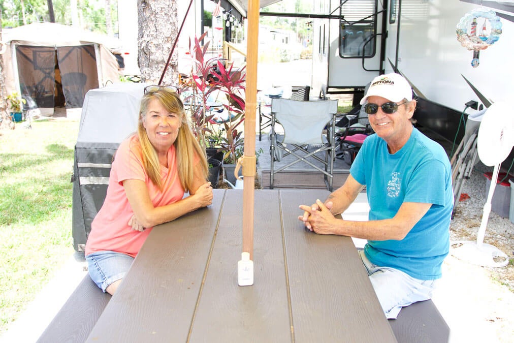 Fulltime Blueway RV Park guests Laurie Byrne and Roger Ferreira at a picnic table in front of their RV.