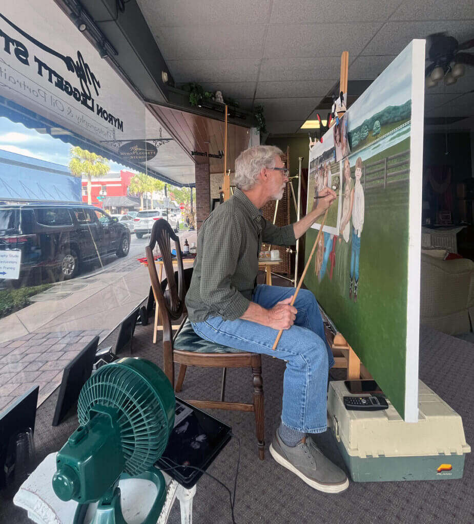 Artist and business owner Myron Leggett in downtown Leesburg, FL painting in storefront window.
