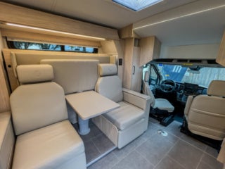 Interior view of a camper van showing seats, a table, and the driver's cabin.