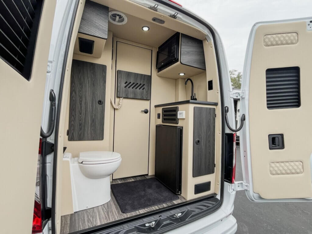 Interior of camper van with back doors open showing a toilet, sink, microwave and storage in the camper van.