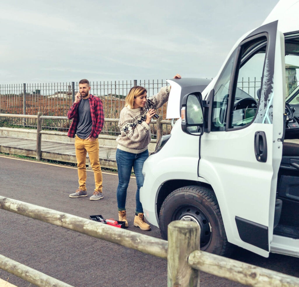Woman repairing broken down campervan while man calls on the phone - Credit: iStock