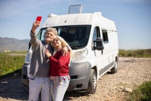 Couple taking a photo on phone outside of a camper van. Photo credit: Pexels