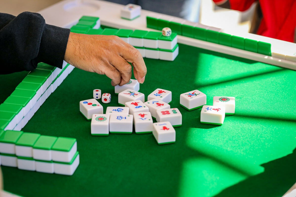 A hand grabbing mahjong tiles during a game of mahjong. Playing on a green felt mahjong board.