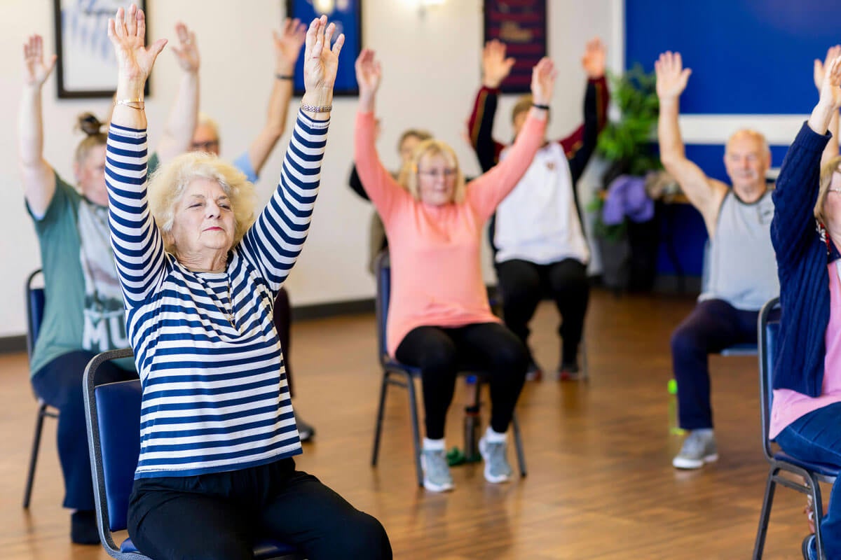 Seniors doing chair aerobics during a group fitness class in an aerobics room.