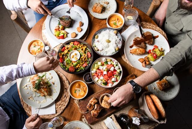 A table full of plates of Mediterranean food. Men's hands are grabbing for a variety of different plates.