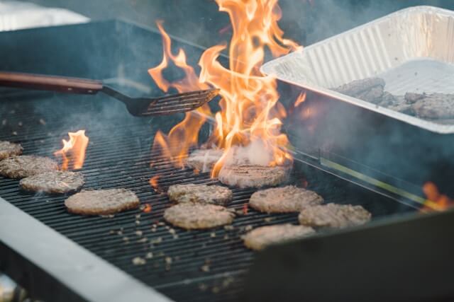 Burgers being cooked on the grill with a flame and spatula.