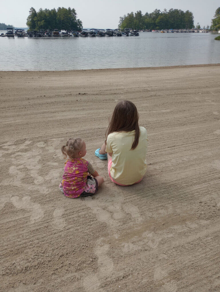 Siblings sitting on the sandy beach at Point Sebago Resort in Maine.