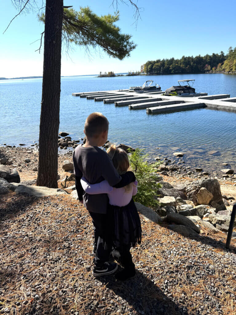 Kids cuddling along the shoreline of Sebago Lake in Maine looking at boat slips.
