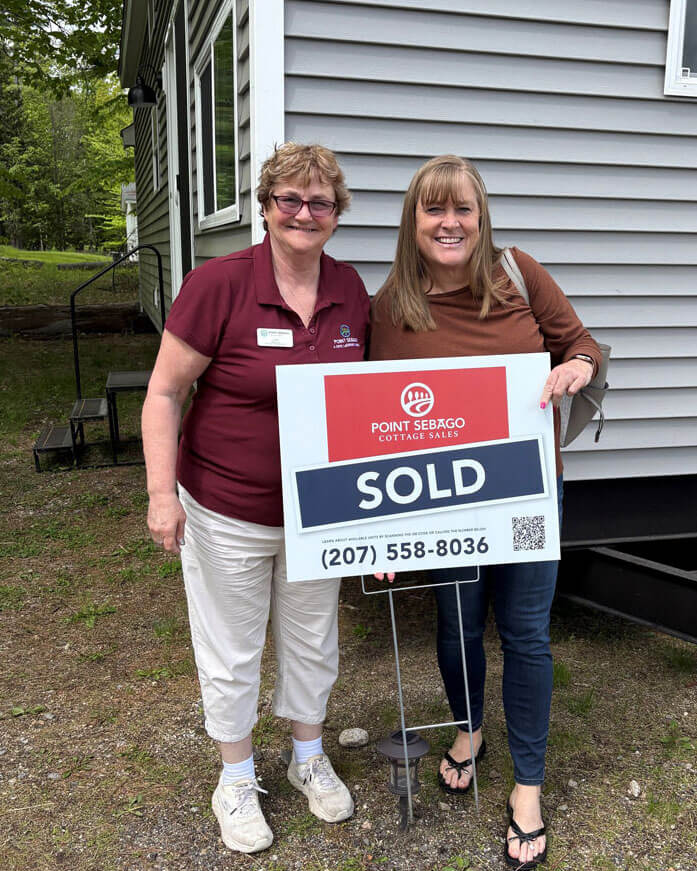 Lori Galford and a Point Sebago guest holding a SOLD sign in front of a Maine cabin.