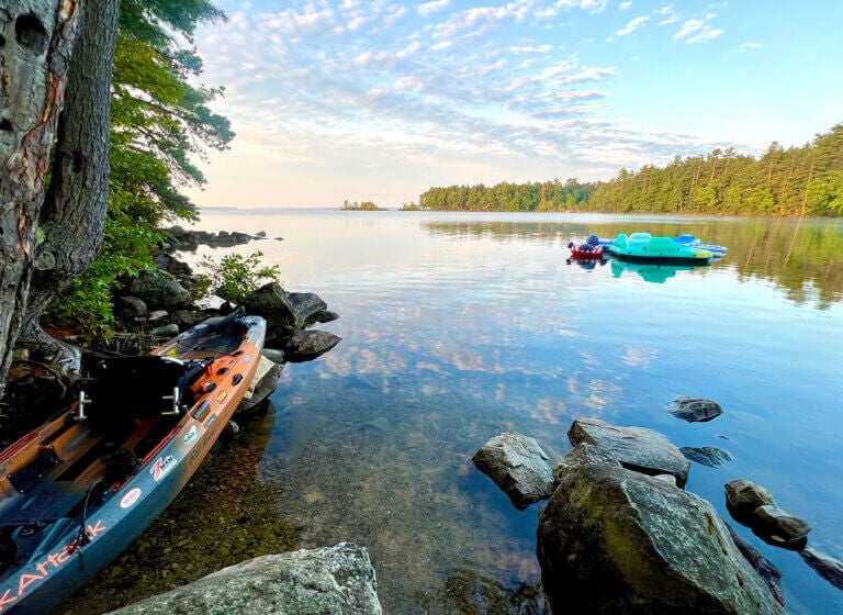 A kayak along the shoreline of Sebago Lake in Maine with inflatable tubes in the background.