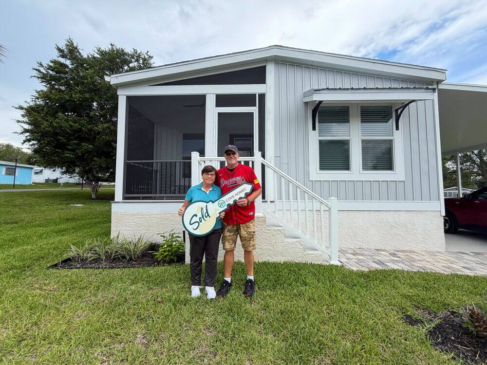 New 55+ homeowners on the front lawn at their new home with a large sign in the shape of a house key that says "SOLD!"
