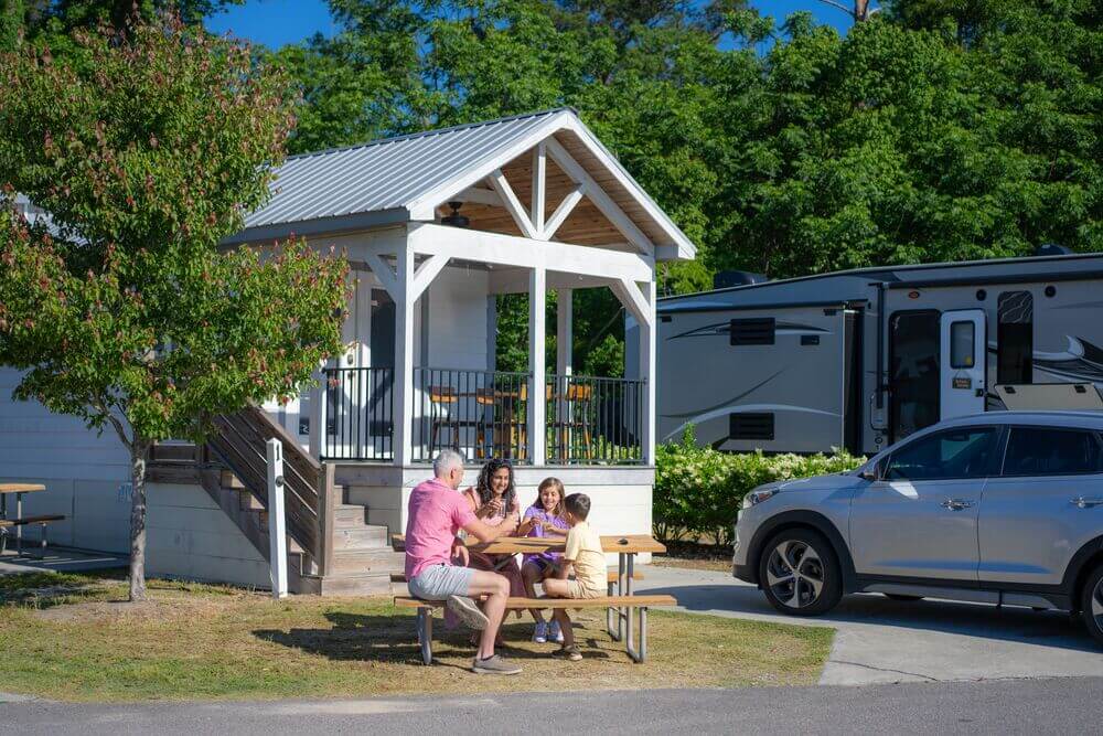 Family sitting around a picnic table in front of a cabin at CreekFire RV Resort in Savannah, Georgia