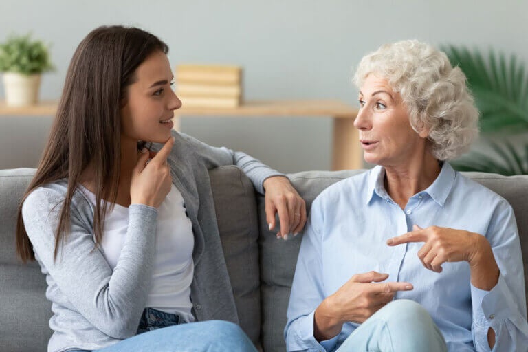 A granddaughter and grandma are sitting on the couch, talking.