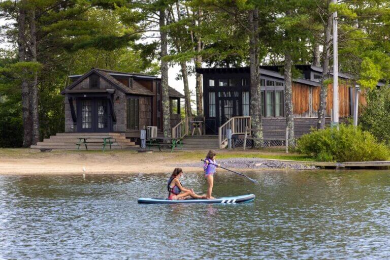 Two people kayaking past cabins at Point Sebago Resort in Casco, Maine.