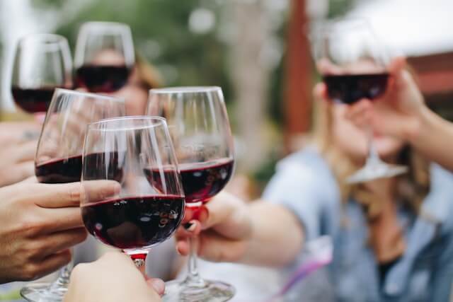 Friends clinking wine glasses together full of red wine.