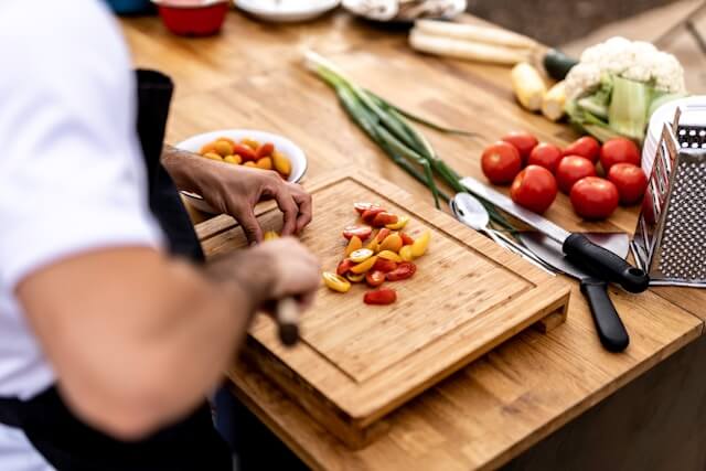 Chef chopping up cherry tomatoes on a wooden cutting board in a kitchen.