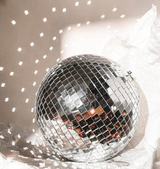 A disco ball is lying on a white sheet, with light reflecting off of it onto the wall.