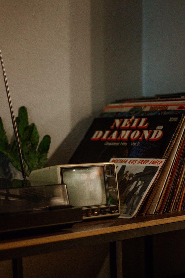 A radio, a mini TV, and records on a bookshelf. A Neil Diamond record is in the front.