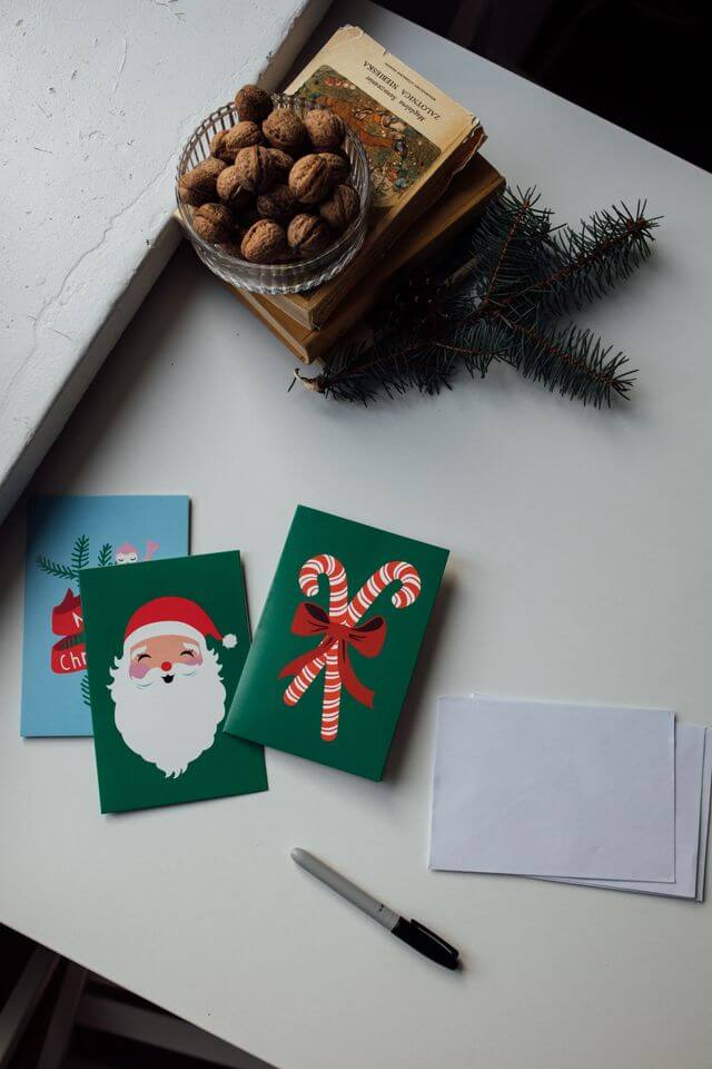 Various Christmas cards, pens, walnuts, and walnuts on a table near a window.